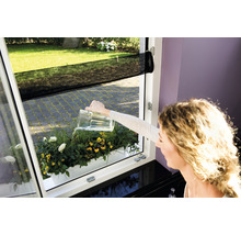 Žena zalévá truhlík s květinami konví na okně se sítí proti hmyzu