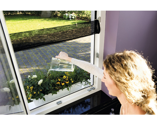 Žena zalévá truhlík s květinami konví na okně se sítí proti hmyzu