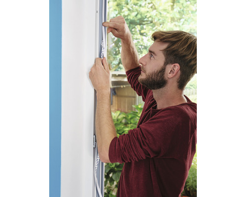 Muž připevňuje těsnicí pásku na rám okna.