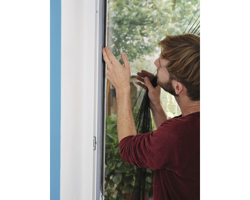 Muž připevňuje síť proti hmyzu na okenní rám.