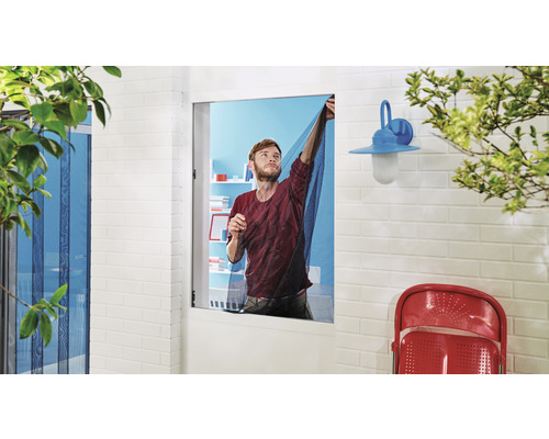 Muž připevňuje na okno síť proti hmyzu, aby se zabránilo vniknutí hmyzu