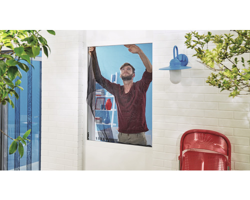 Muž montuje moskytiéru na okno, aby zabránil vniknutí hmyzu.