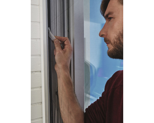 Muž upevňuje síť proti hmyzu na okenní rám