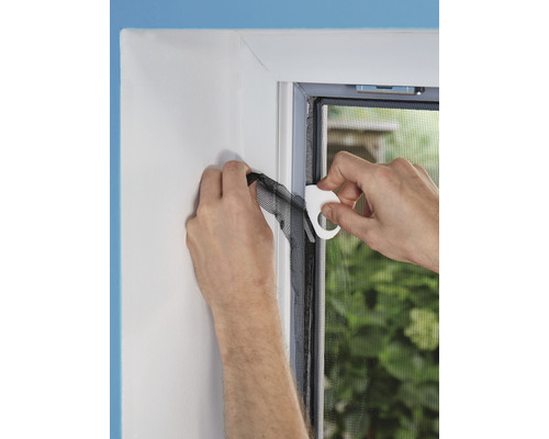 Osoba připevňuje síť proti hmyzu k okennímu rámu pomocí montážního nástroje.