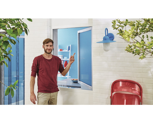 Muž stojí před oknem se sítí proti hmyzu a ukazuje na ni.