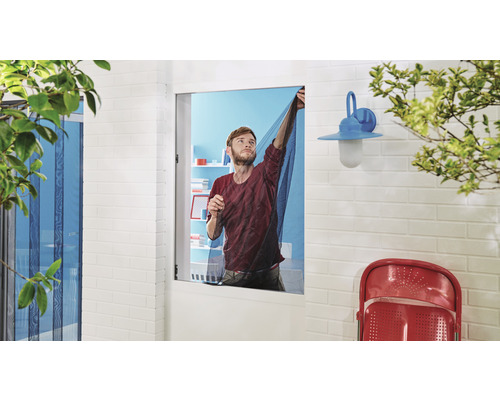 Muž montuje síť proti hmyzu před oknem.