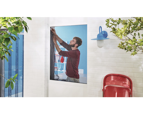 Muž upevňuje síť proti hmyzu na okno.