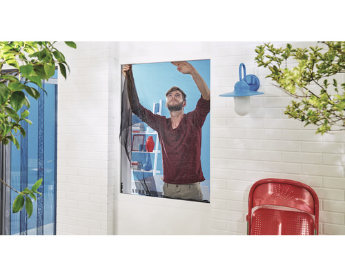 Muž montuje moskytiéru na okno, aby zabránil vniknutí hmyzu.