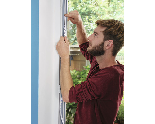 Muž upevňuje těsnicí pásku na okenní rám.