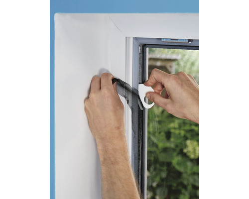 Osoba připevňuje síť proti hmyzu k okennímu rámu pomocí montážního nástroje.