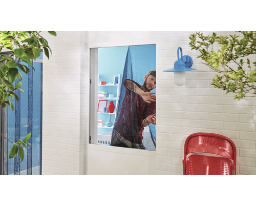 Muž montuje do okna síť proti hmyzu.