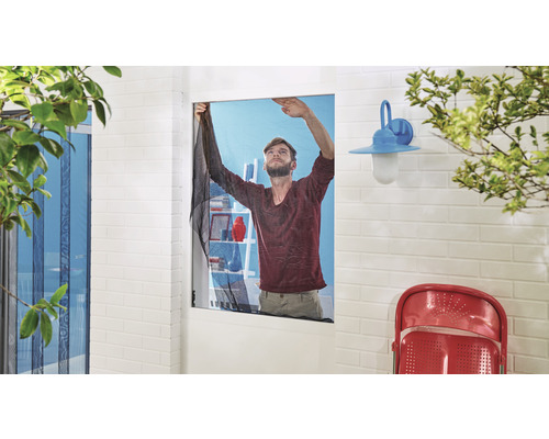 Muž upevňuje síť proti hmyzu na okno