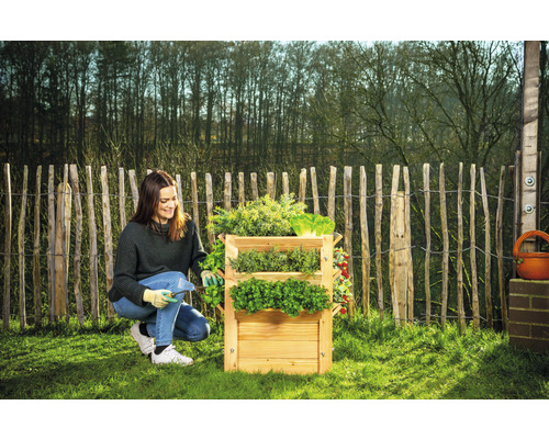 Žena pracuje na dřevěném třípatrovém bylinkovém záhonu na zahradě