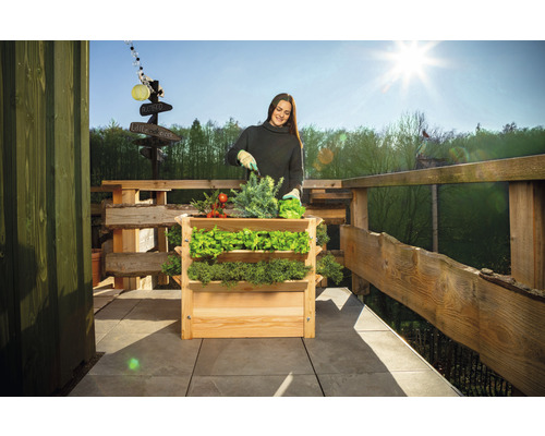 Žena zahradničí ve vyvýšeném záhonu na balkoně s dřevěným plotem.