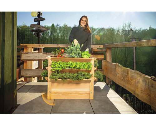 Žena s dřevěným truhlíkem se třemi úrovněmi a různou zeleninou na balkóně.