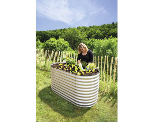 Žena sází rostliny do vyvýšeného záhonu z kovu na zahradě.