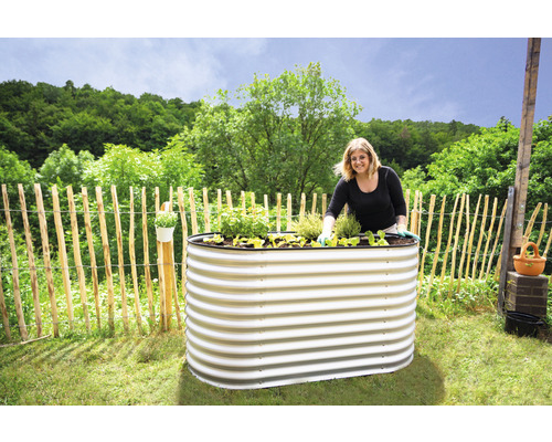 Žena sází rostliny do vyvýšeného záhonu z kovu na zahradě.