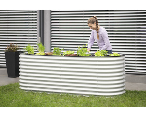 Kovový vyvýšený záhon s rostlinami a ženou, která na něm pracuje