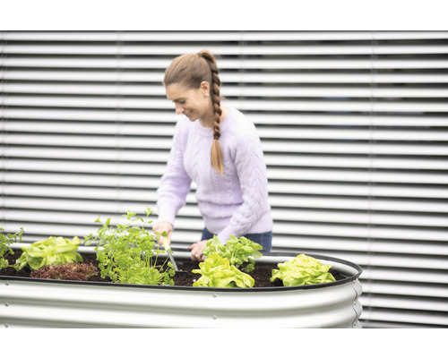 Žena pracuje ve vyvýšeném záhonu se salátem a bylinkami