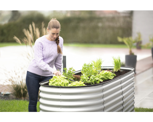 Žena pracuje na zahradě s vyvýšeným záhonem z kovu a různou zeleninou.