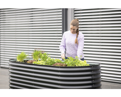 Kovový vyvýšený záhon s rostlinami a žena pracující na zahradě