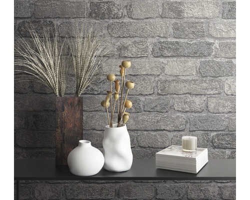 Dekorativní scéna s vázami, rostlinami, svíčkou a stoh knih proti kamenné zdi.