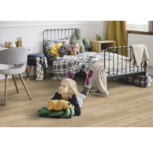 Dítě leží na laminátové podlaze v dětském pokoji s postelí a psacím stolem