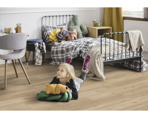 Dítě leží na laminátové podlaze v dětském pokoji s postelí a psacím stolem