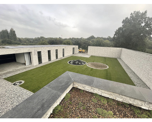 Pohled na moderní zahradu s trávníkem, obklopenou zdmi a moderním domem