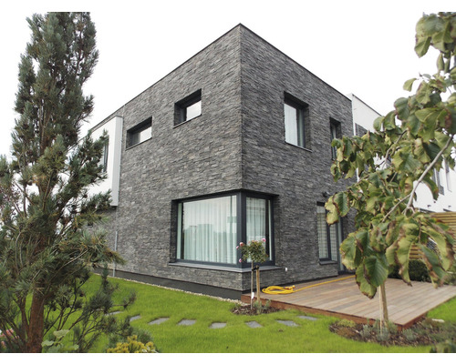 Moderní dům s fasádou s kamenným vzhledem, okny a zahradní úpravou