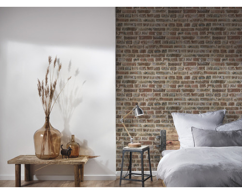 Ložnice s postelí před cihlovou zdí a dekorací na dřevěném stole