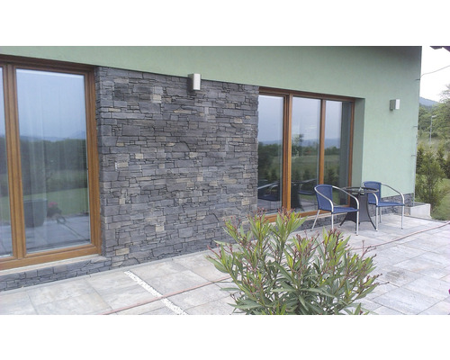 Fasáda domu s okny a obkladem z přírodního kamene a terasa se zahradním nábytkem