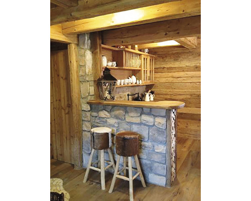 Rustikální bar s kamenným obkladem, dřevěnou pracovní deskou a dvěma barovými stoličkami s kožešinovým potahem v dřevěné chatě.
