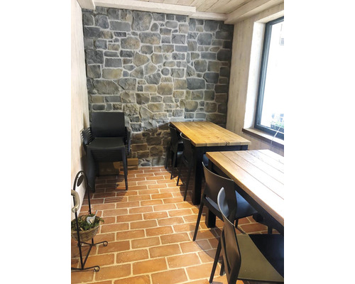 Interiér s kamennou dekorativní stěnou, stoly a židlemi na cihlové podlaze