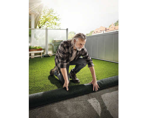 Muž pokládá umělý trávník na terase.