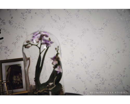 Detail stěny s květinovou tapetou a orchidejí pod skleněným poklopem.