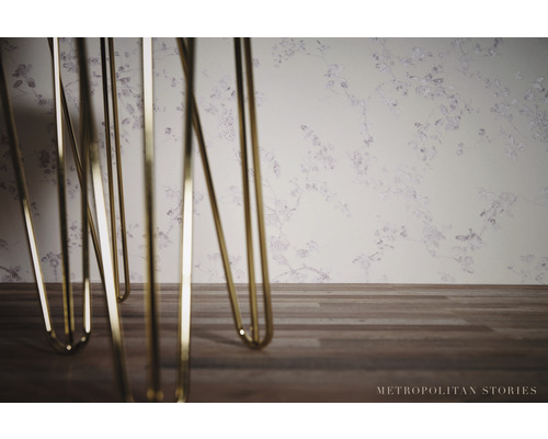 Detailní záběr kovových nohou stolu před tapetou se vzorem květin.