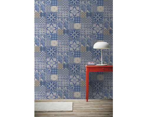 Pokoj s vzorovanou tapetou ve stylu patchwork, červeným stolem a lampou