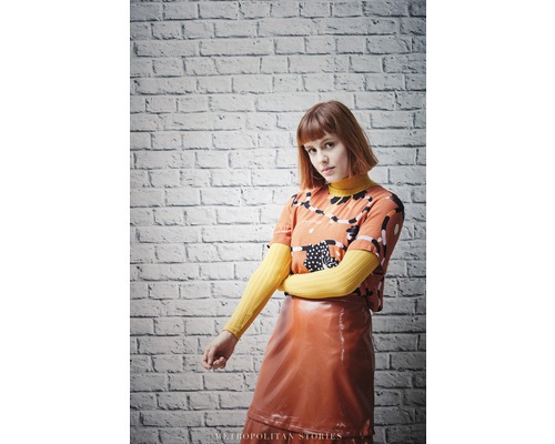 Žena s tričkem se vzorem a lesklou sukní před cihlovou zdí