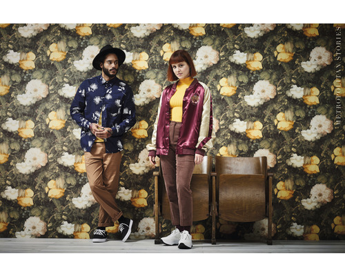 Dvě osoby pózují před stěnou s květinovým dekorem