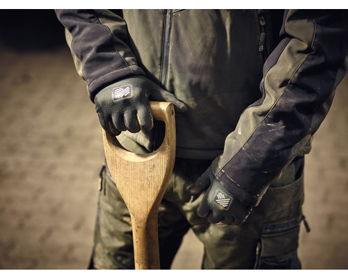 Osoba v pracovním oděvu drží rýč s dřevěnou rukojetí a má na sobě pracovní rukavice.
