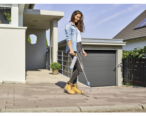 Žena odstraňuje plevel odstraňovačem plevele před domem.