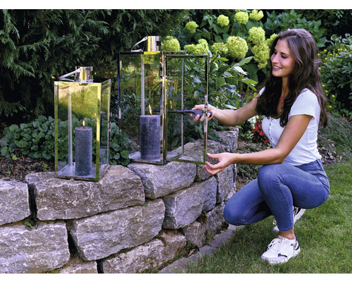 Žena zapaluje svíčku ve svícnu na kamenné zídce v zahradě