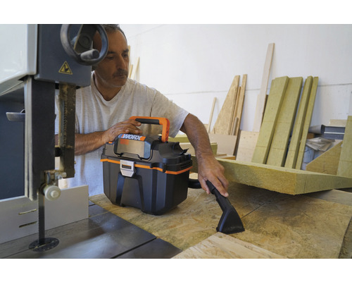 Řemeslník používá mokro-suchý vysavač na dílenském stole s pásovou pilou a zbytky dřeva