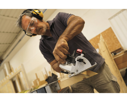 Muž řeže dřevěnou desku mini ruční okružní pilou a má přitom ochranné brýle a chrániče sluchu.