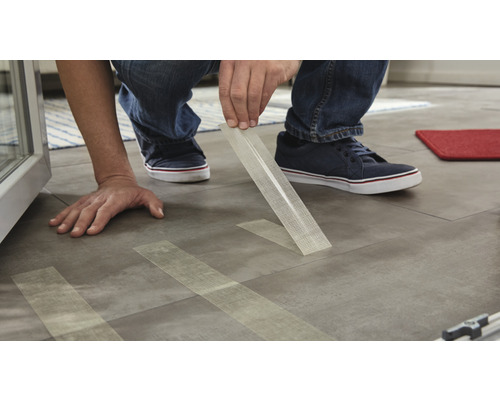 Muž pokládá dlaždice pomocí lepicí pásky pro upevnění