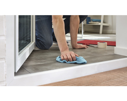 Osoba utírá hadrem podlahu v blízkosti okna.