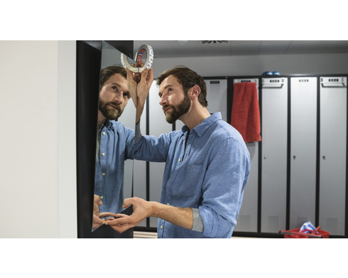 Muž připevňuje zrcadlo oboustrannou lepicí páskou v šatně