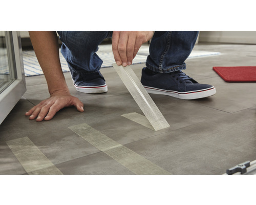 Osoba pokládá samolepicí vinylové dlaždice na podlahu.