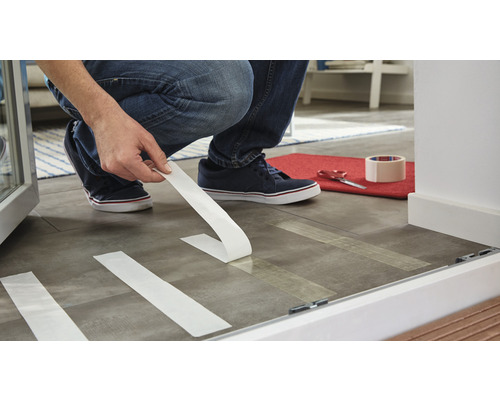 Osoba připevňuje lepicí pásku na podlahu k přípravě oblasti.